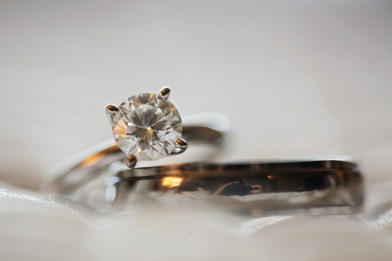 a solitaire round cut diamond ring sits with a wedding band on a white fabric.