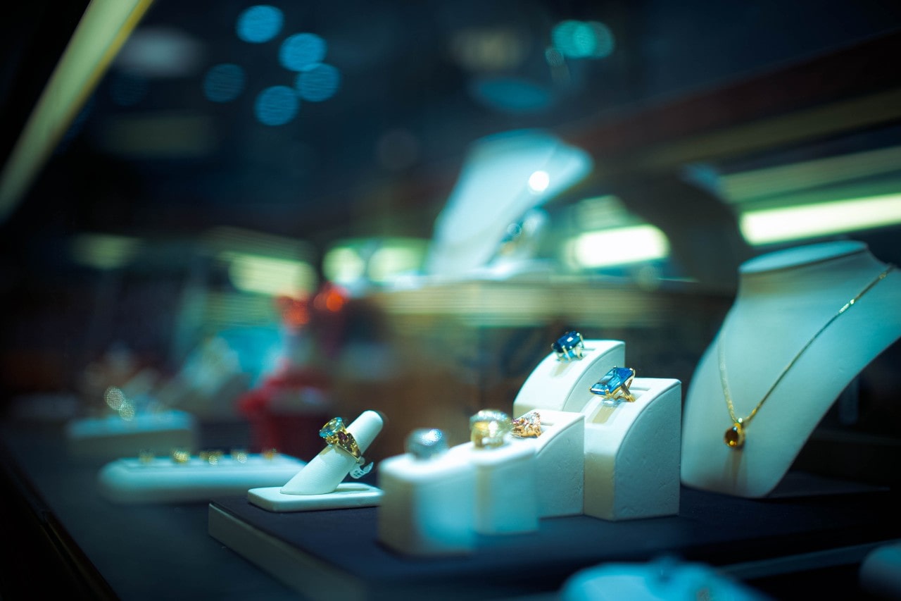 A view of a jewellery store display under night lighting featuring colorful gemstone necklaces and rings.