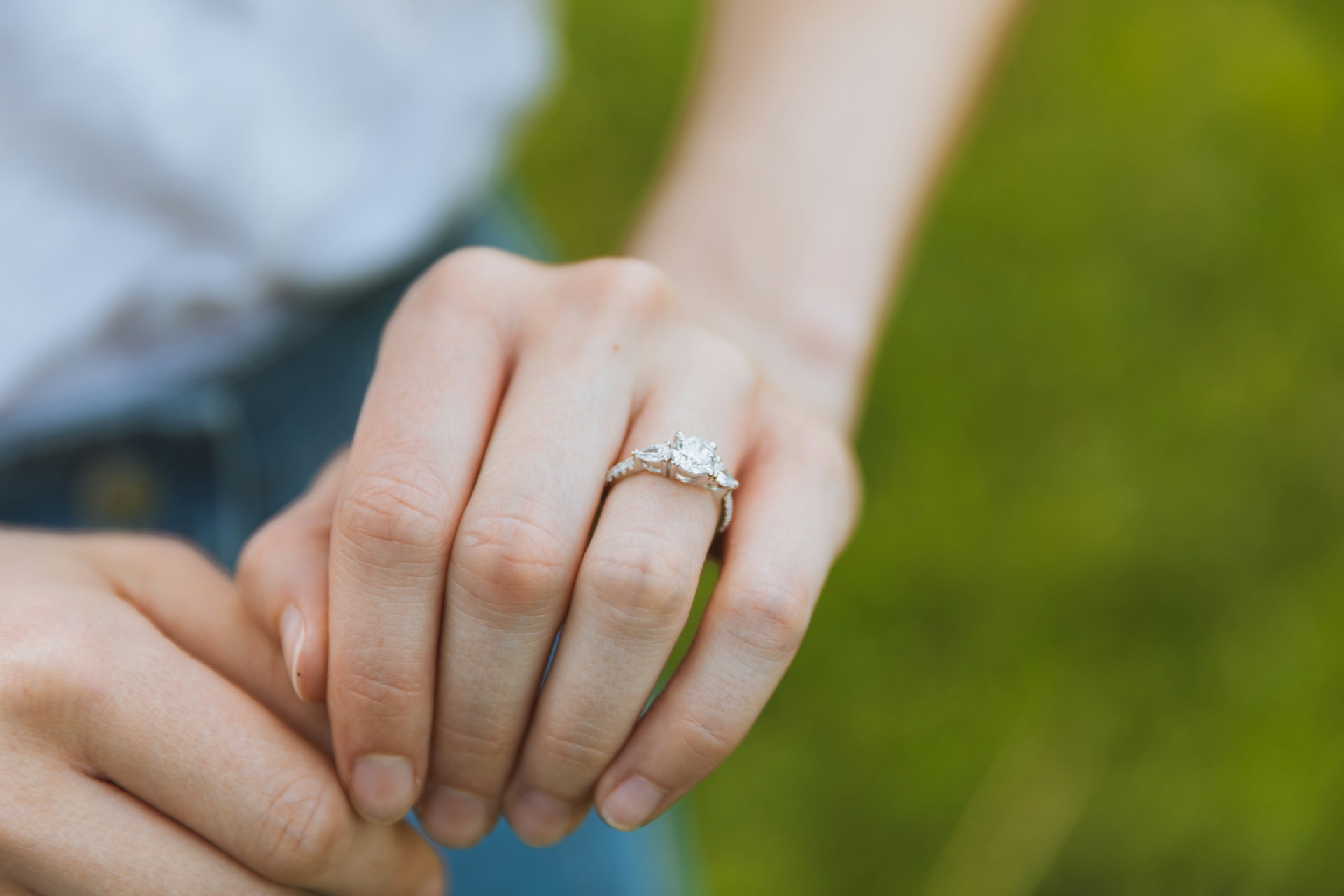 A close-up of a woman’s hand, an elegant three-stone engagement ring on her finger.