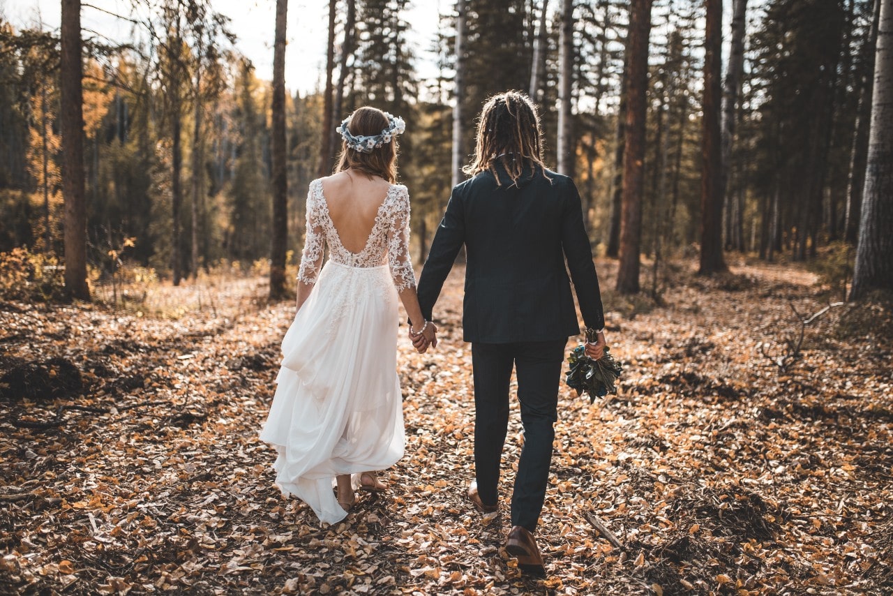 A bride and groom walk through a fall forest.