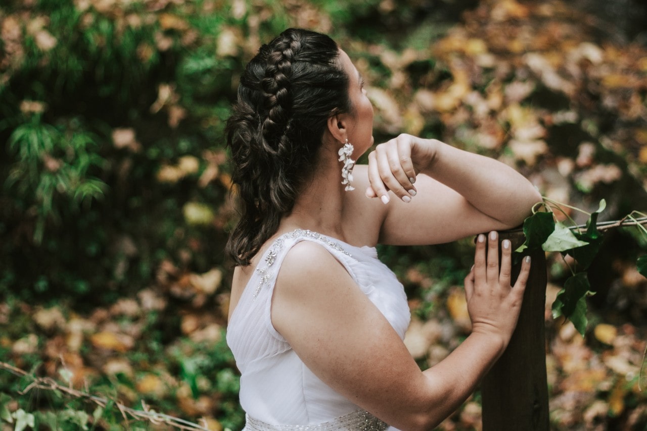 A bride leans against a fence post, looking off into the distance.