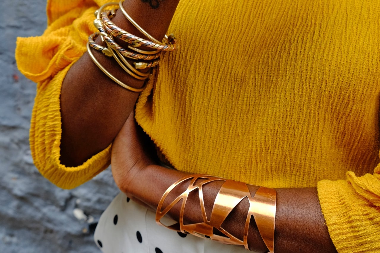 A close up of a woman&rsquo;s hands adorned with several yellow gold cuffs.