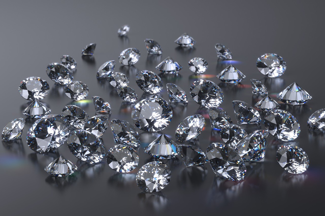 A cluster of sparkling diamonds scattered on a reflective surface, capturing light and creating colorful reflections.
