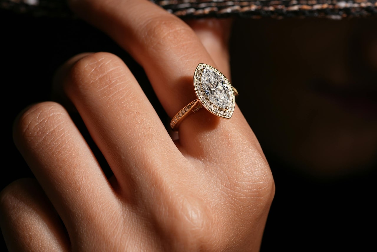 Close-up of a hand wearing a gold ring with an oval-shaped, sparkling diamond.