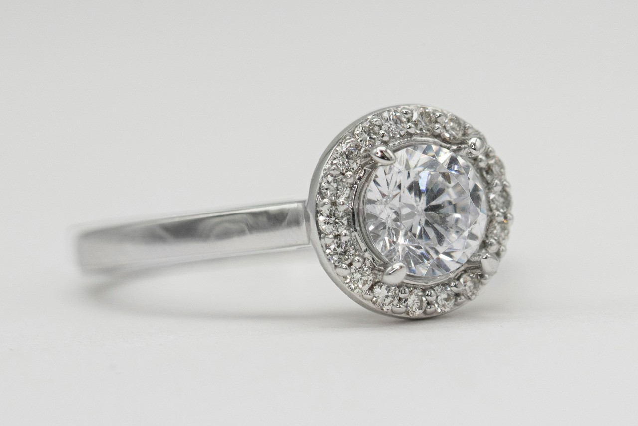 Silver halo engagement ring with a central round diamond surrounded by smaller sparkling diamonds, set on a thin polished band.