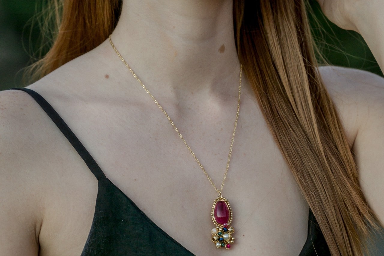 Close up of a woman wearing a thin gold chain with a ruby pendant.