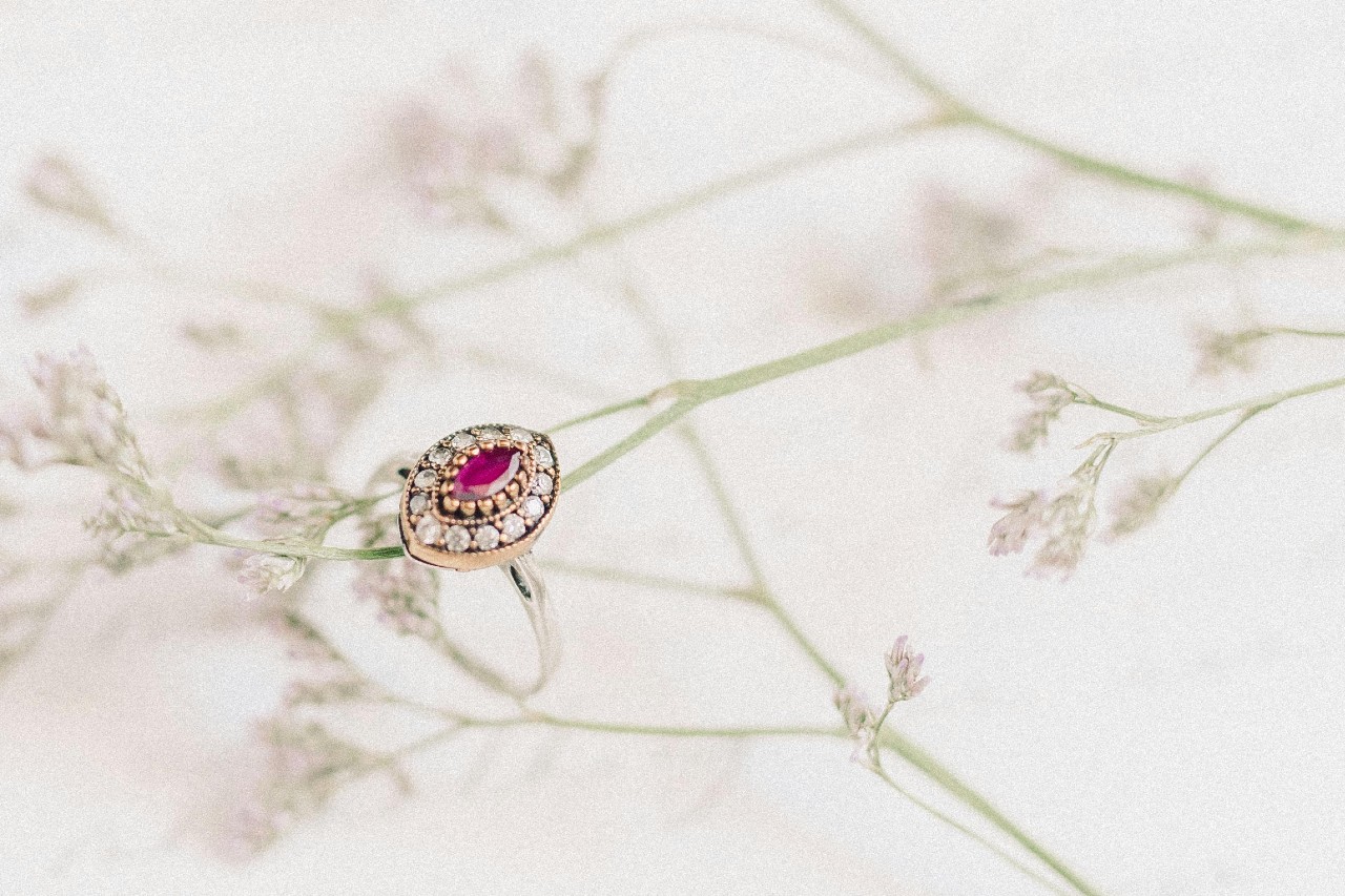Oval ruby ring surrounded by diamonds on a floral background.