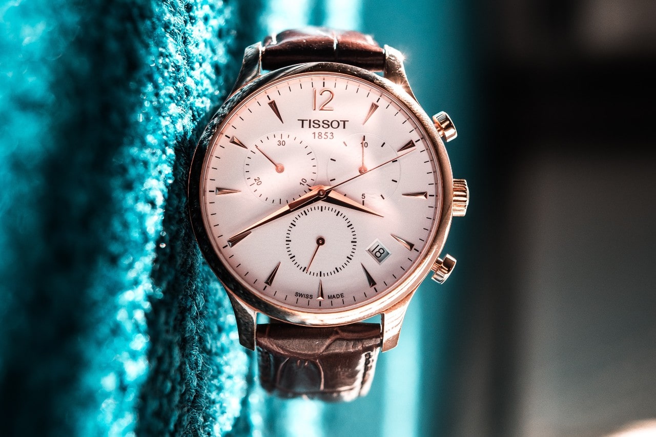 A Tissot watch with a white dial and brown leather strap lying on a green fabric.