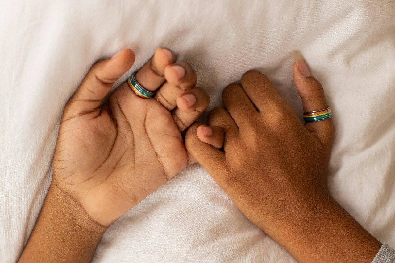 a couple’s hands locking pinkies and wearing the same rainbow ring