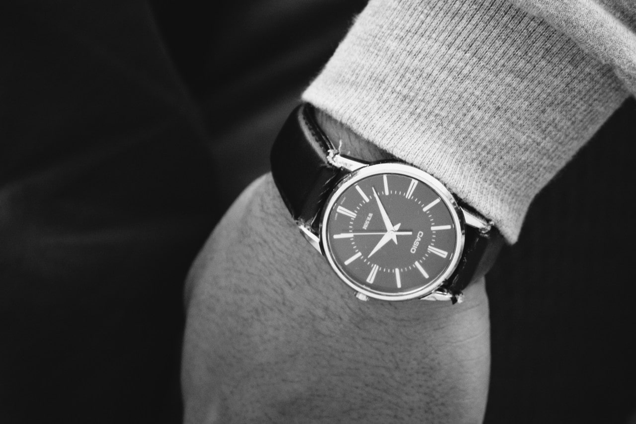 A black and white picture of a person's wrist adorned with a classic black leather-strap Casio watch
