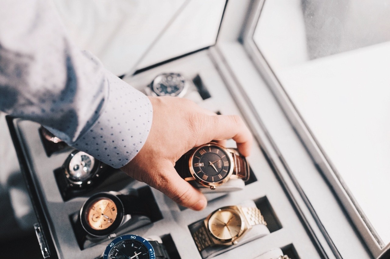 A person reaching into a watch display case, selecting a rose gold wristwatch.
