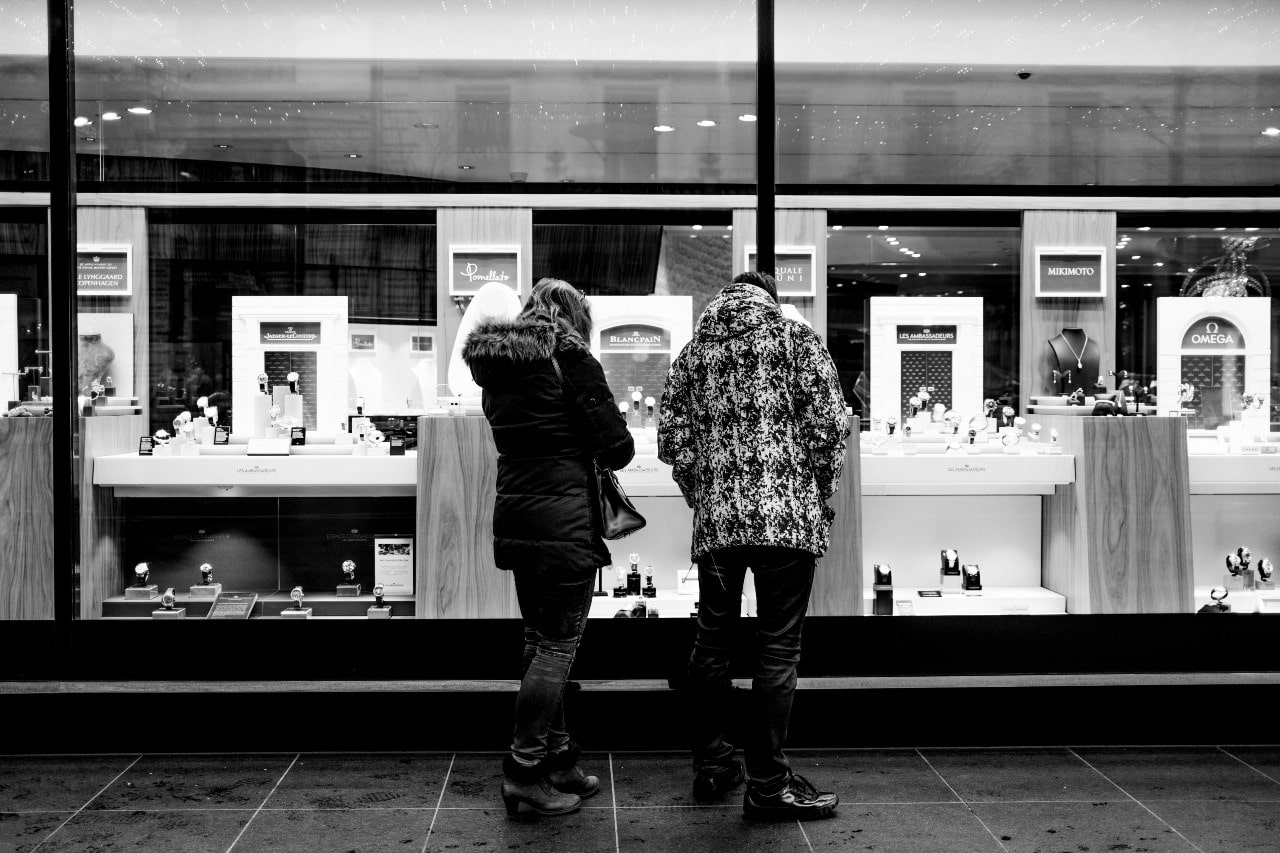 A black and white image of a young couple window shopping at their local jewelry store.