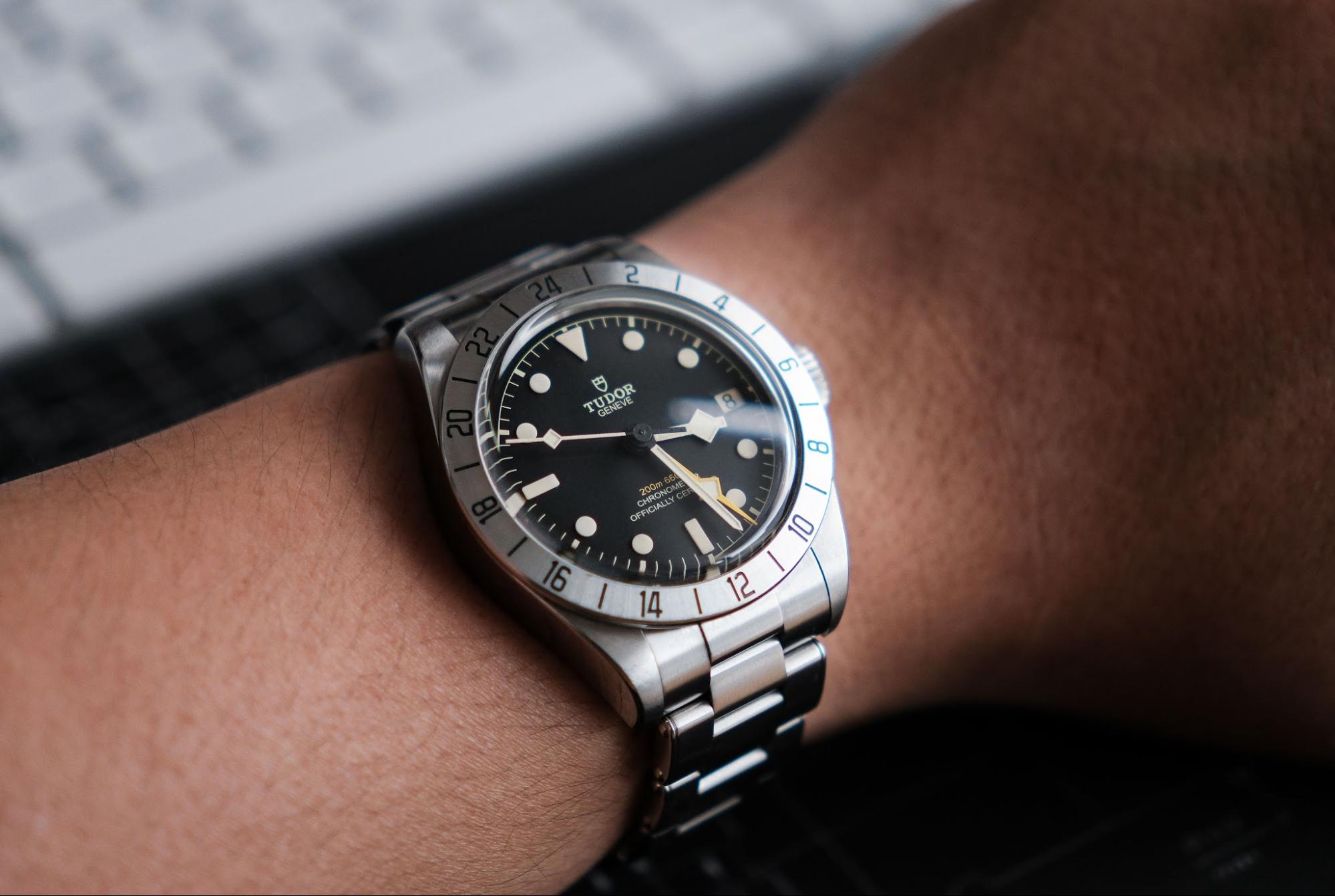 Close-up wrist shot of a TUDOR Black Bay Pro GMT luxury watch featuring a stainless steel bracelet, and a matte black dial with a prominent yellow GMT hand.