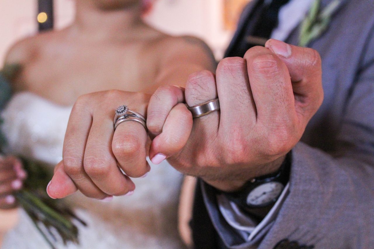 A bride and groom link pinkie fingers, showing off their bridal jewellery.