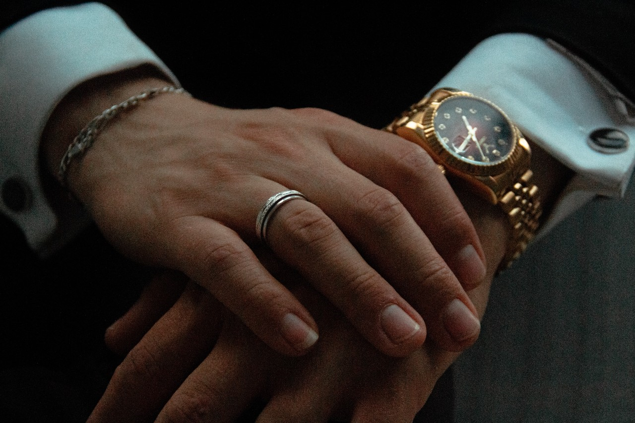 man’s hands clasped and wearing a luxury watch and jewellery
