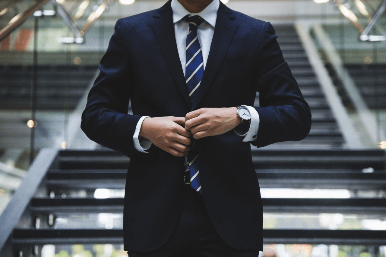 man in a suit wearing a luxury watch as he walks down the stairs to a lobby.