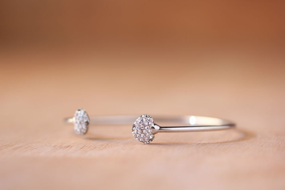 A delicate bracelet with two round, diamond-studded ends rests on a light wooden surface.
