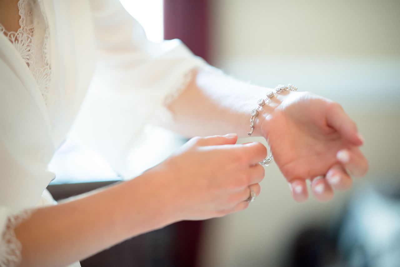 A woman in a white lace robe gently fastens a delicate tennis bracelet on her wrist.