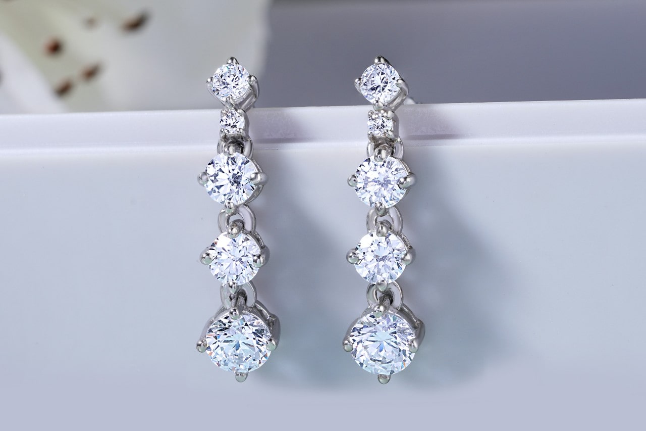 Two sparkling diamond drop earrings are displayed against a light background, each earring featuring a line of round brilliant cut diamonds. Two sparkling diamond drop earrings are displayed against a light background, each earring featuring a line of round brilliant cut diamonds.