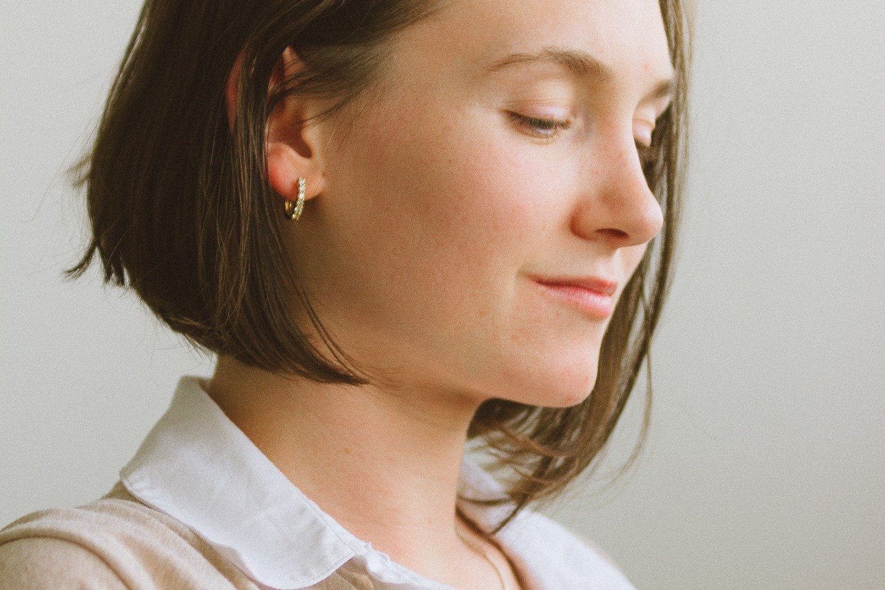 A woman with short brown hair wearing small gold hoop earrings, looking downward. A woman with short brown hair wearing small gold hoop earrings, looking downward.