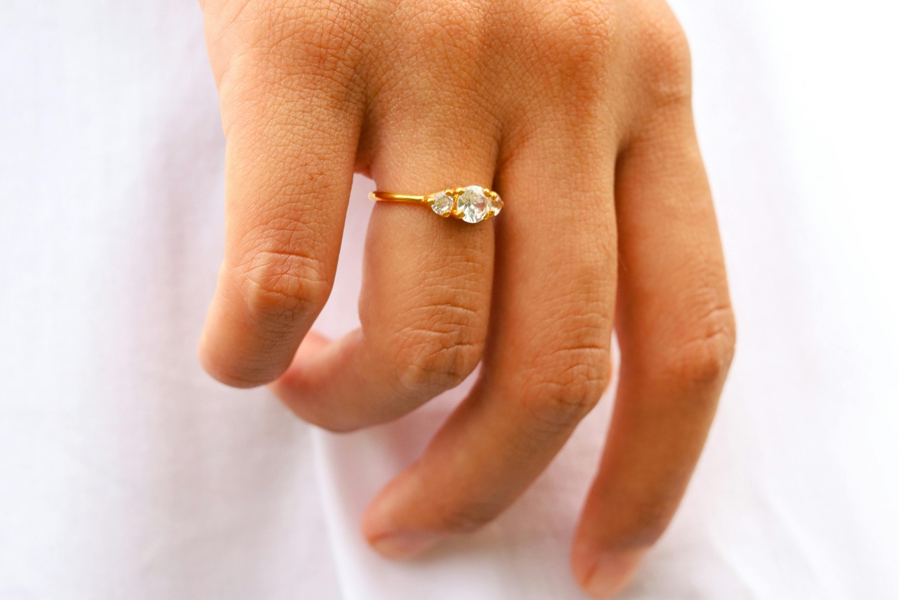 A close-up of a hand with a yellow gold three stone engagement ring.