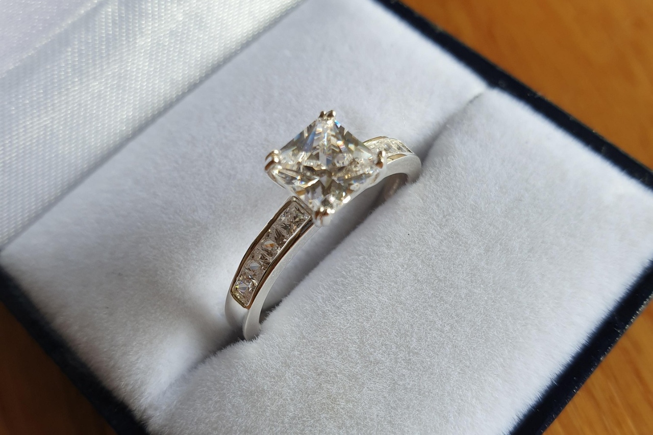 A close-up of a princess cut engagement ring with a side stone setting sat in a velvet ring box.