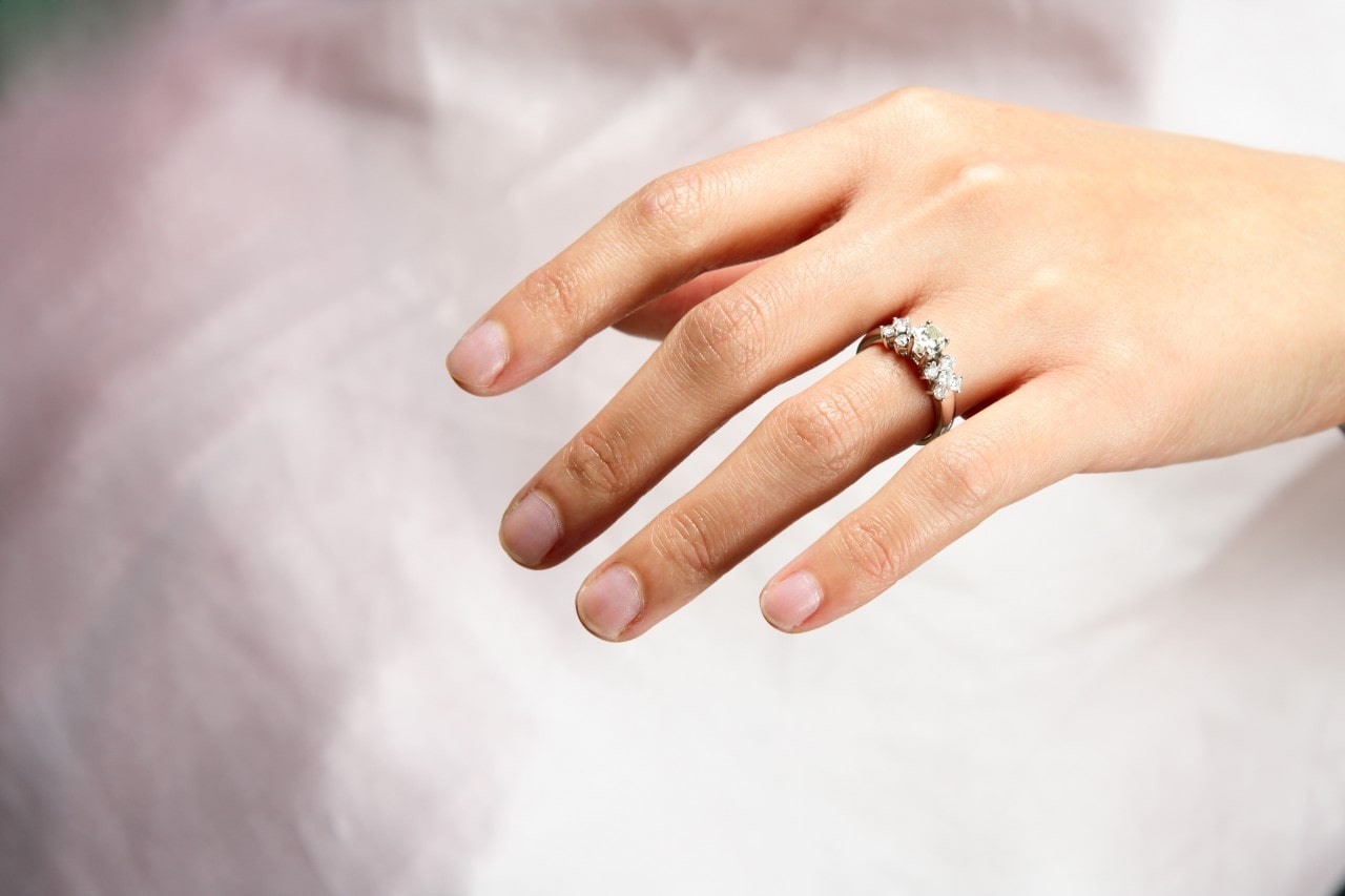 Close-up of a hand adorned with a glistening diamond engagement ring against a soft white backdrop.