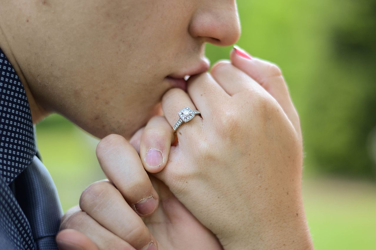 Close-up of a person gently kissing a hand wearing an engagement ring against a soft green background.