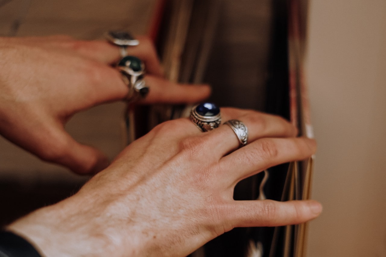 a pair of hands looking through records and wearing a number of chunky white gold rings