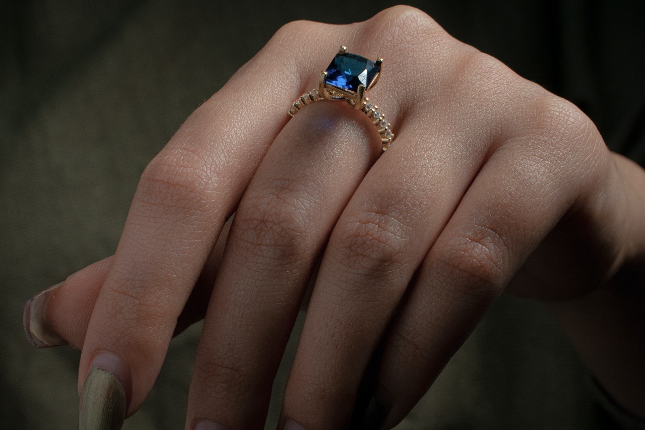 a close up image of a hand wearing a yellow gold fashion ring featuring a sapphire stone