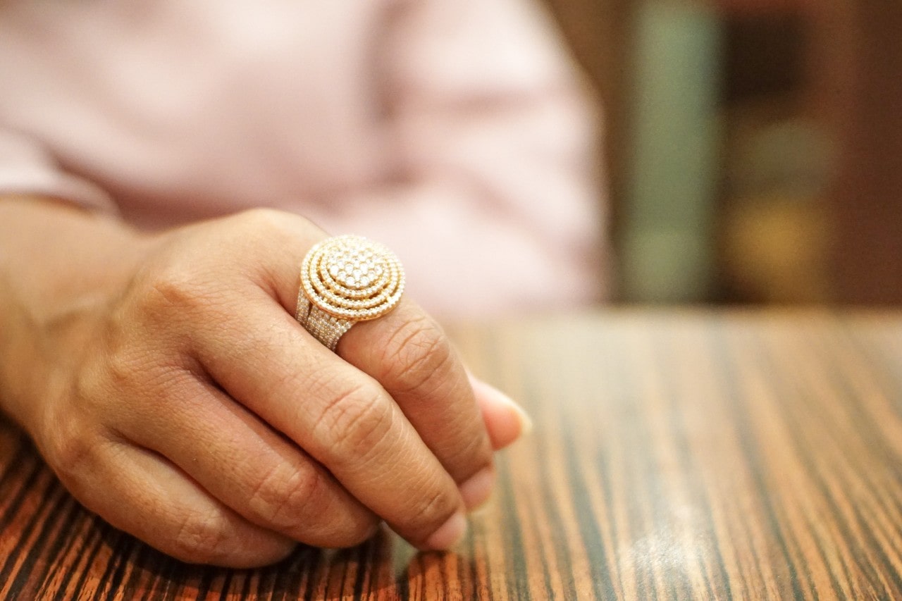 A woman rests her hand on a table, wearing an ornate diamond fashion ring.