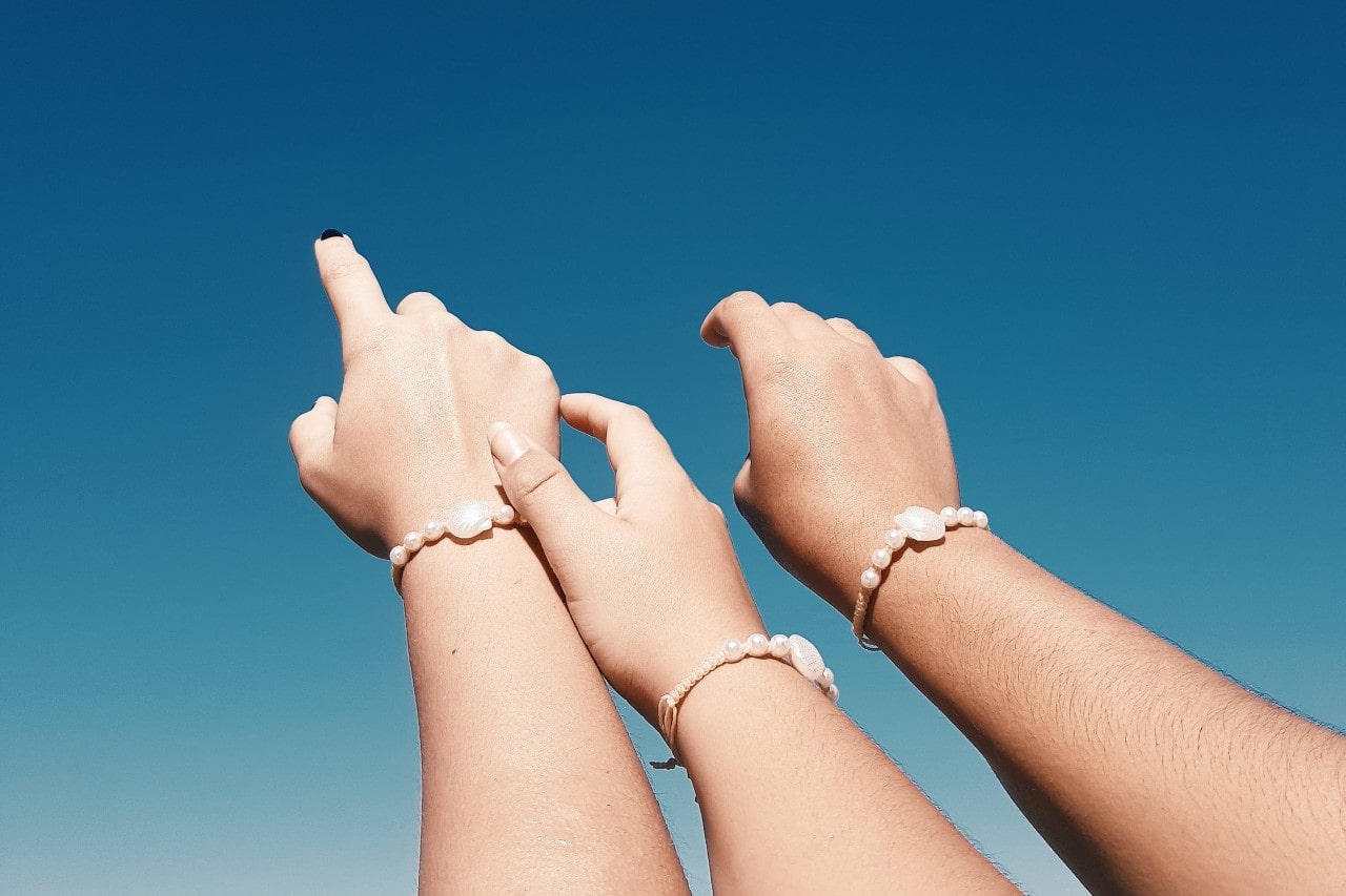 three women's outstretched arms wearing natural shell bracelets.