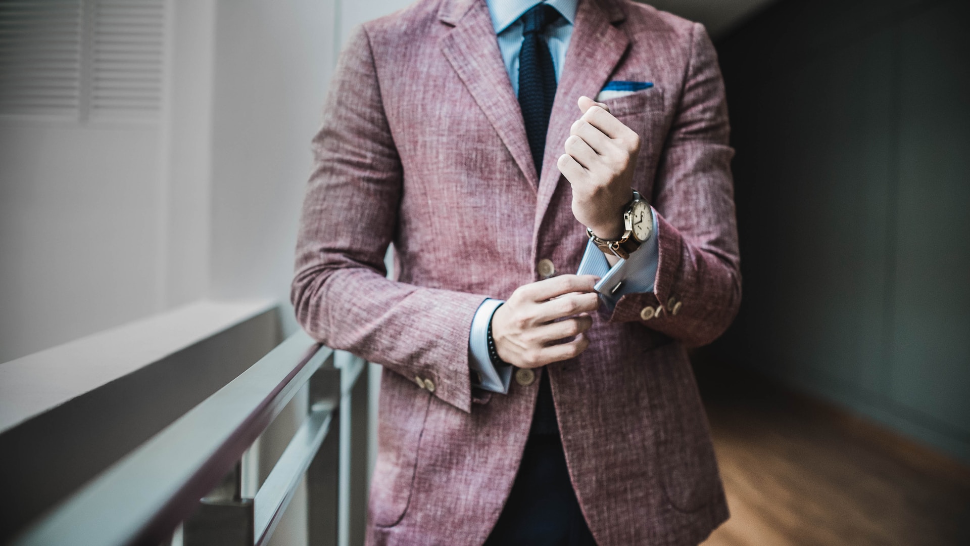 A man in a pink suit fixing his cufflinks, showcasing his leather wristwatch.