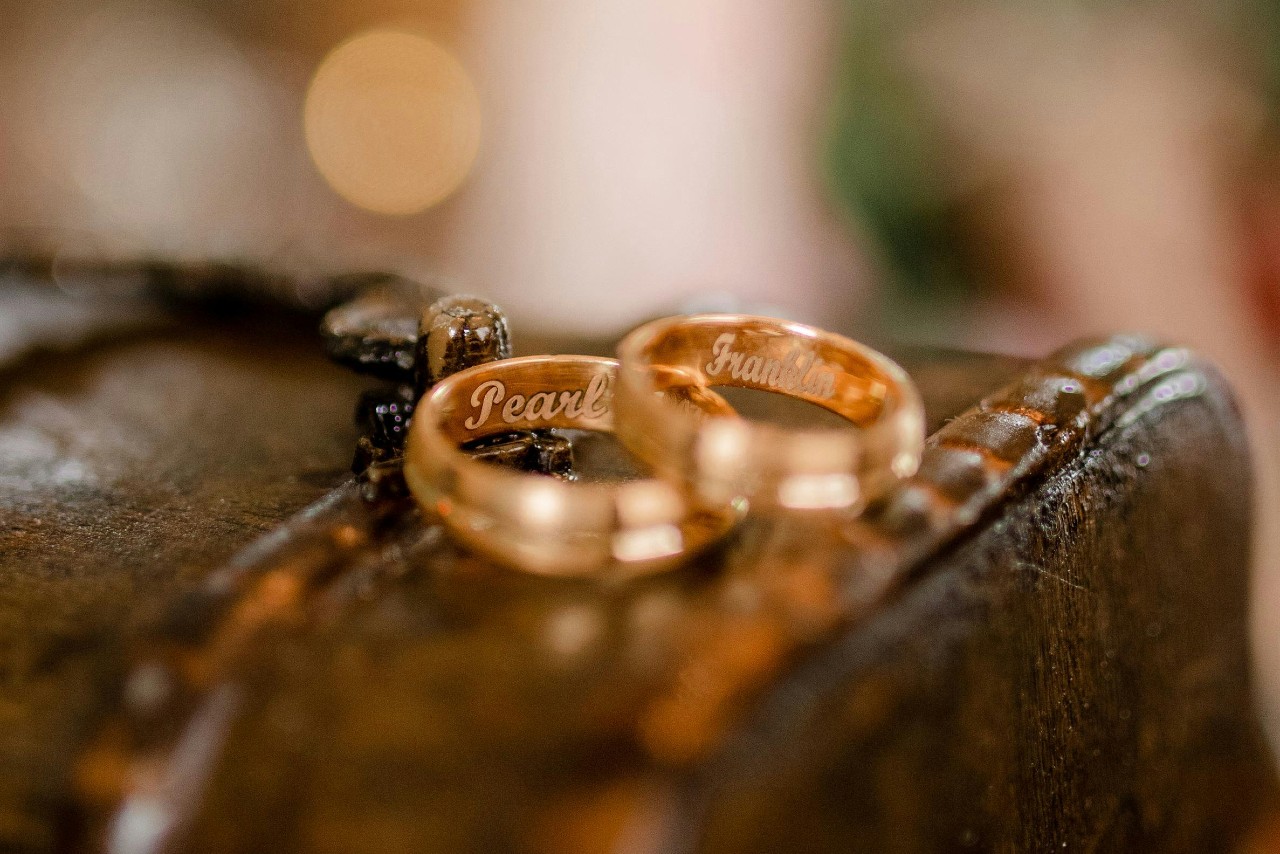 Two yellow gold wedding bands with engraved names inside, on top of the wooden surface.