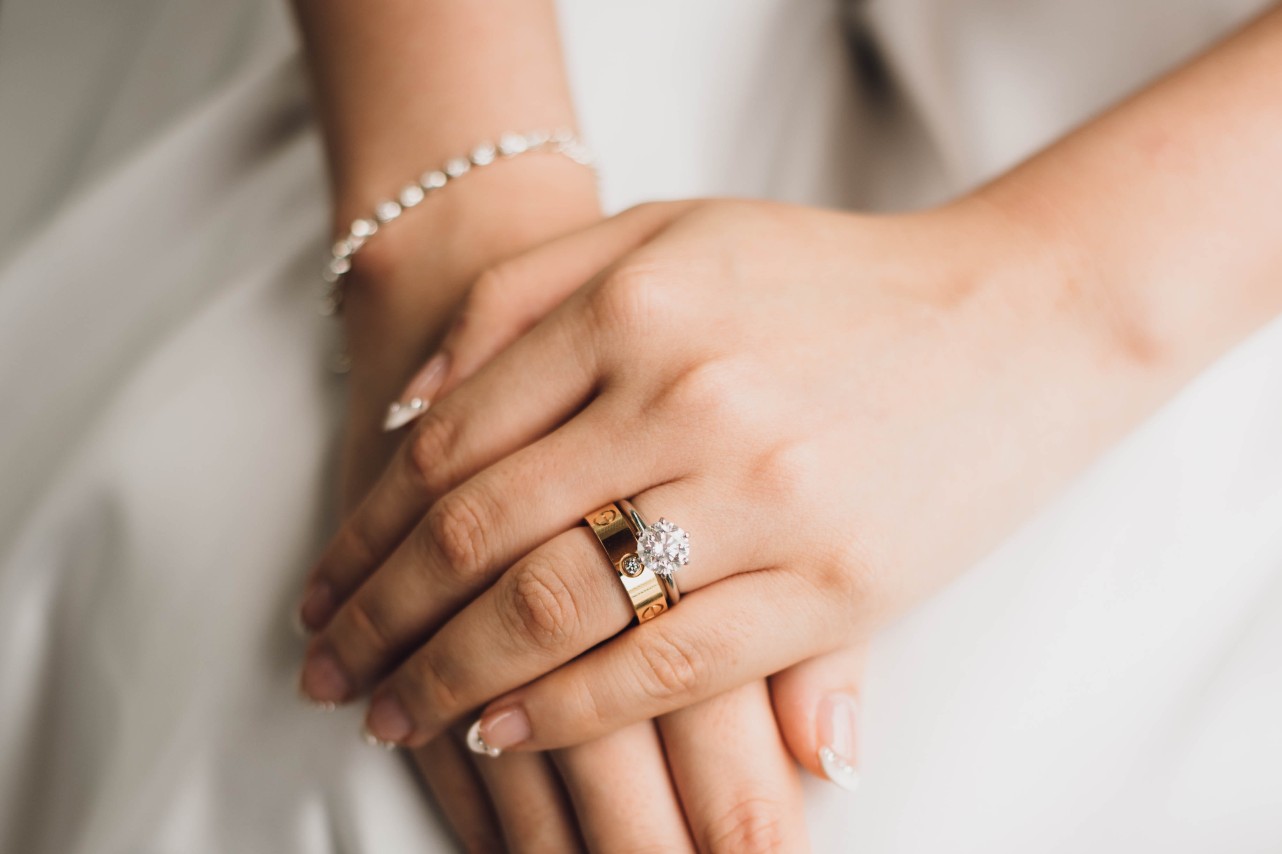A close up of the bride's hands, showcasing a yellow gold wedding band and diamond engagement ring.