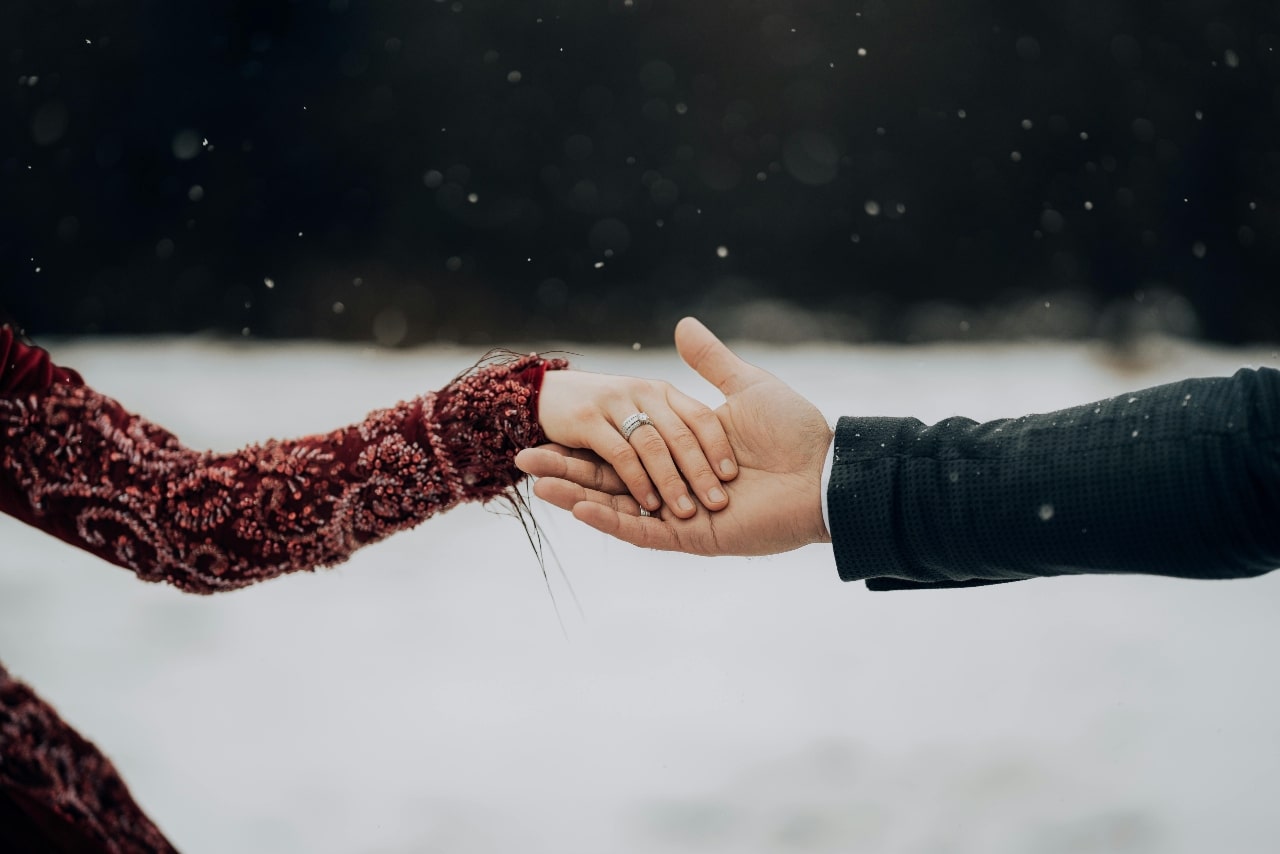 Two hands against a snowy background, showcasing white diamond wedding band on a woman’s hand.