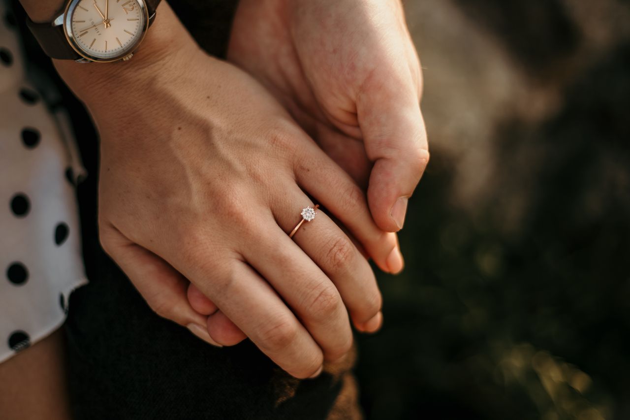 A close up of a shiny gold engagement ring on a woman’s hand.