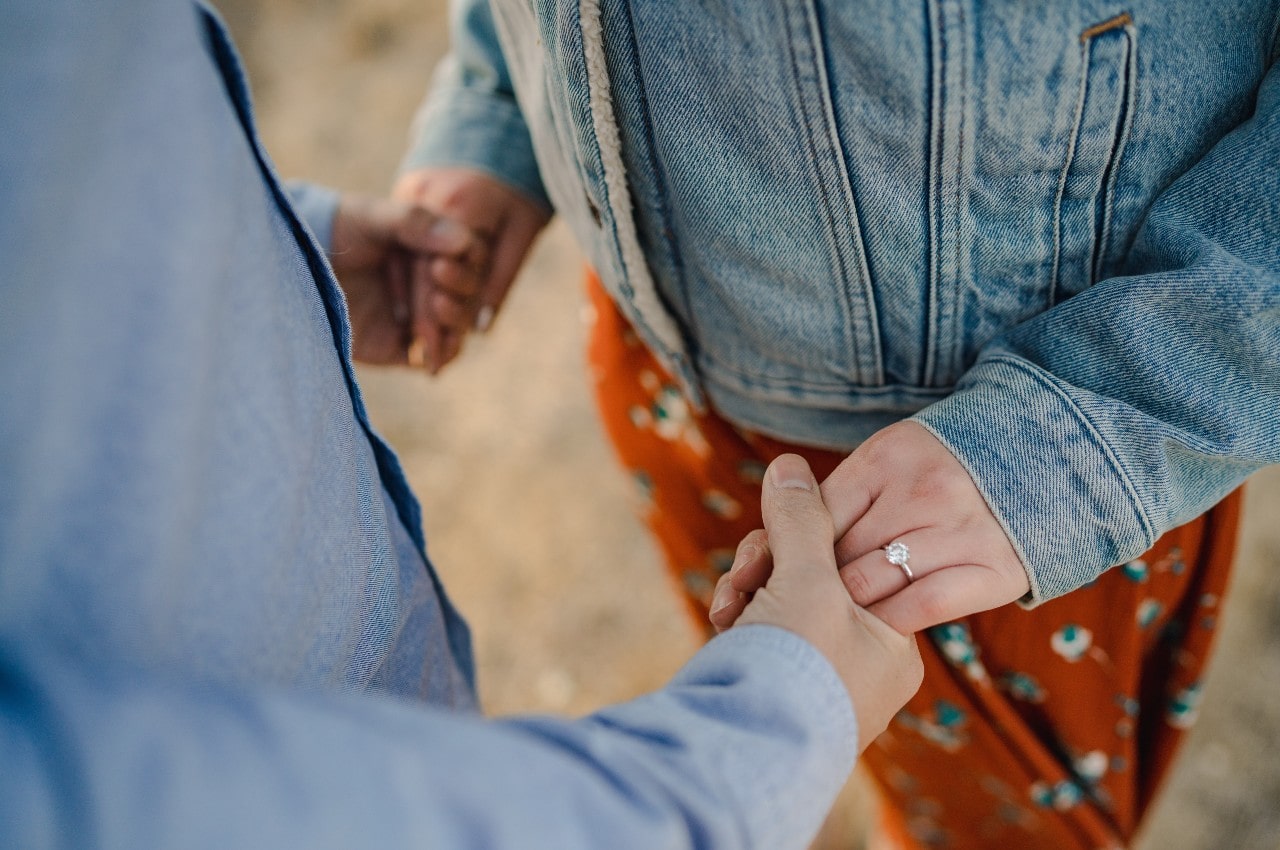 A woman wearing a beautiful engagement ring while holding her partner's hands.