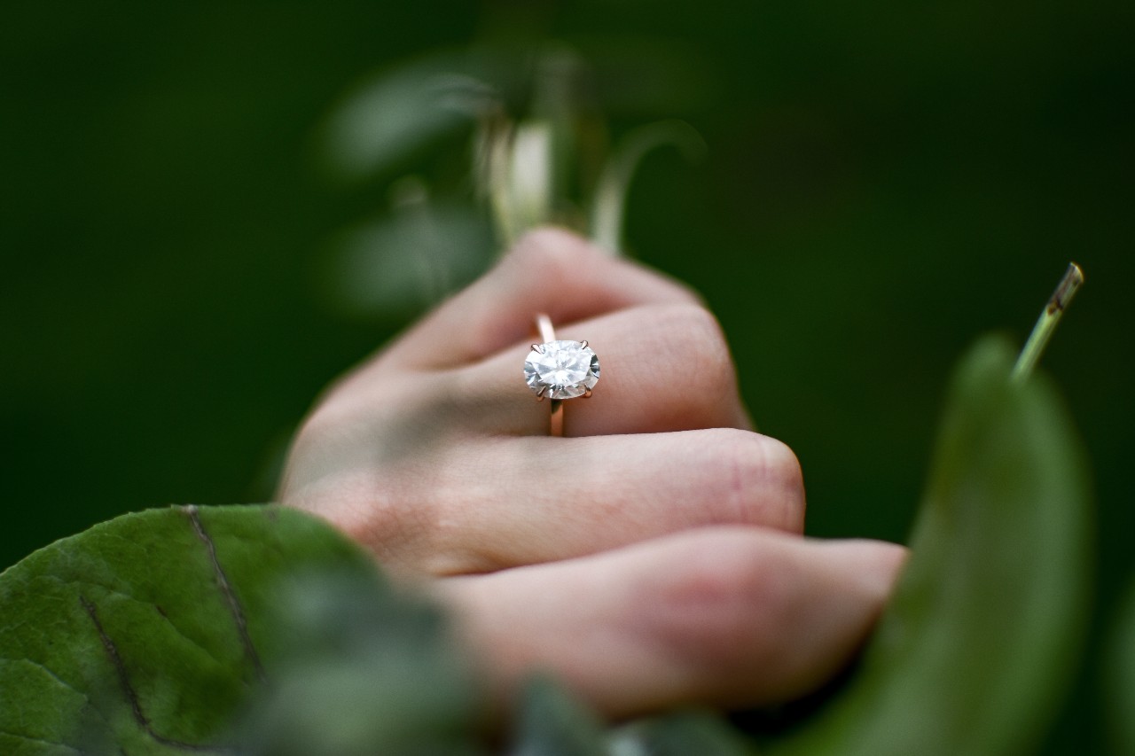 a woman wearing a yellow gold solitaire ring holds onto a branch.