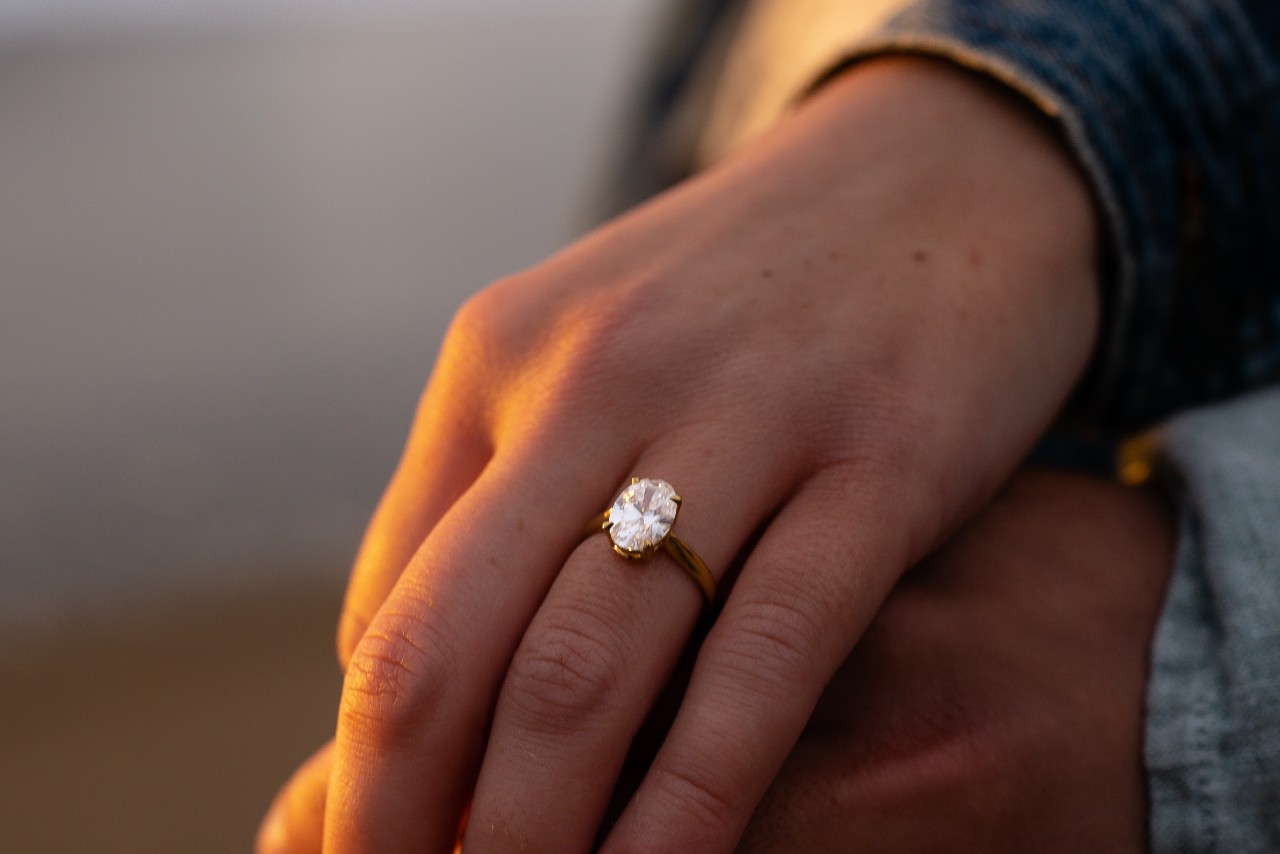 a woman wearing a solitaire engagement ring holds her partner’s hand.
