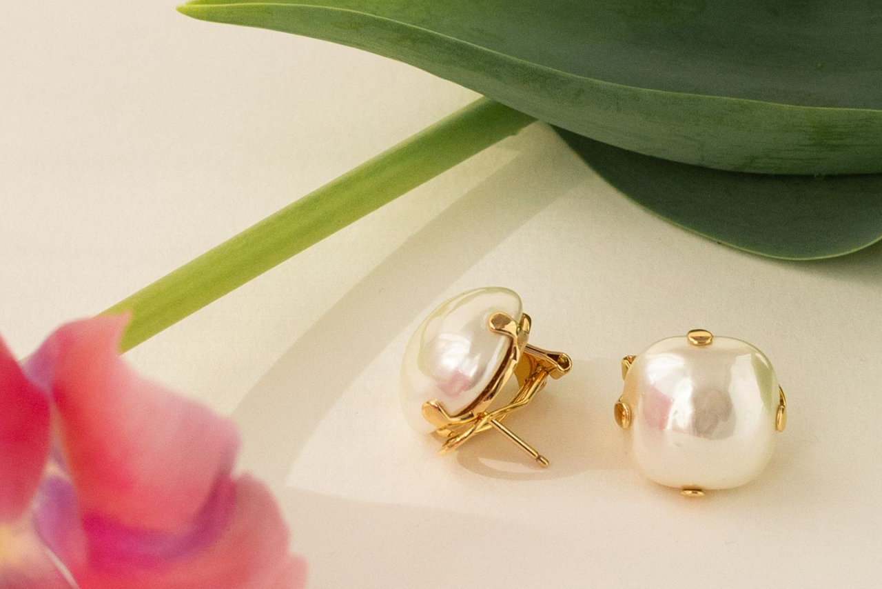 Yellow gold pearl studs near the tulip on a beige surface.