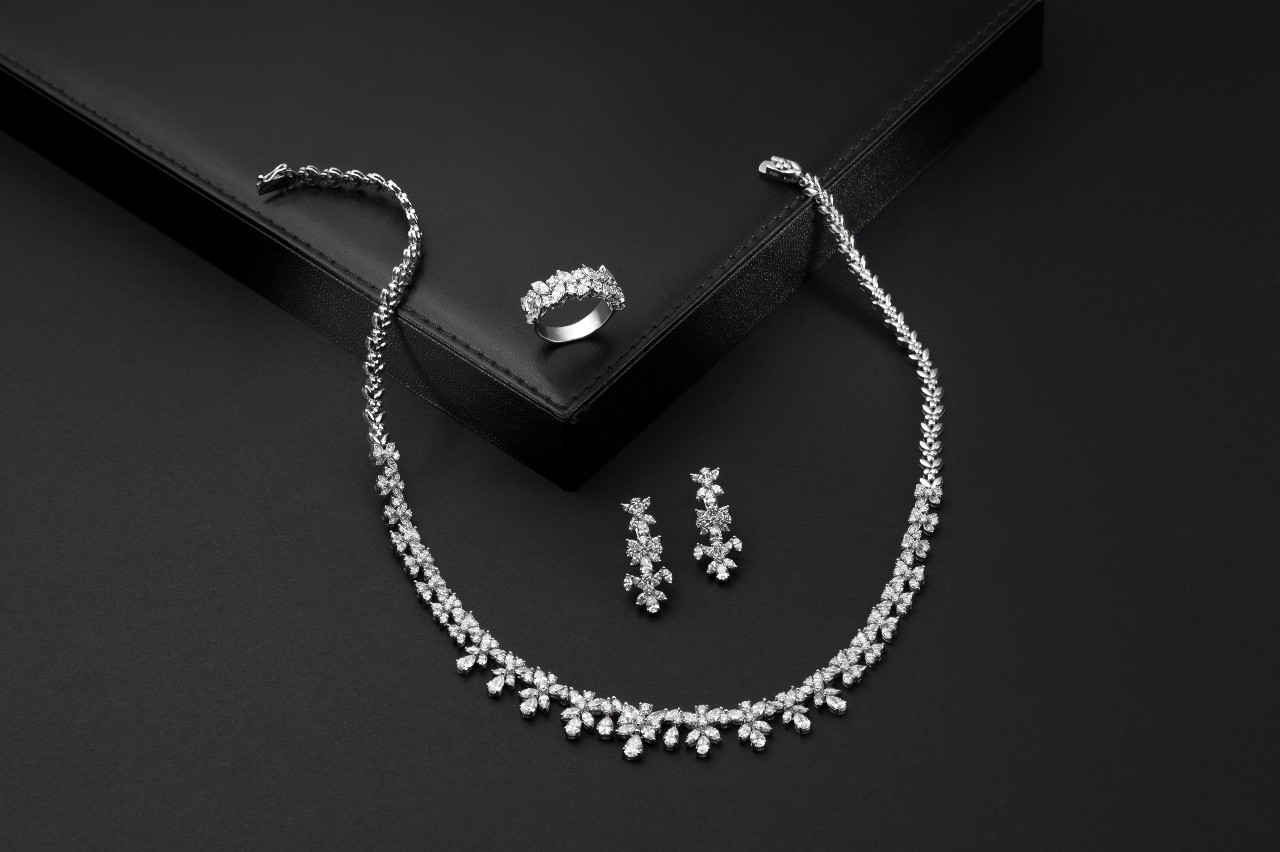 A white gold diamond jewellery set displayed on a black surface, featuring a necklace, earrings, and a matching ring.