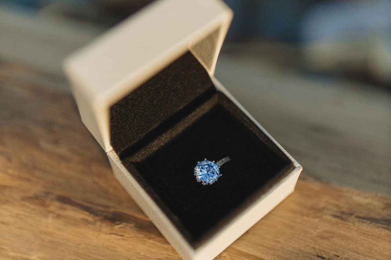 A close-up of an engagement ring with a blue centre stone in a white ring box.