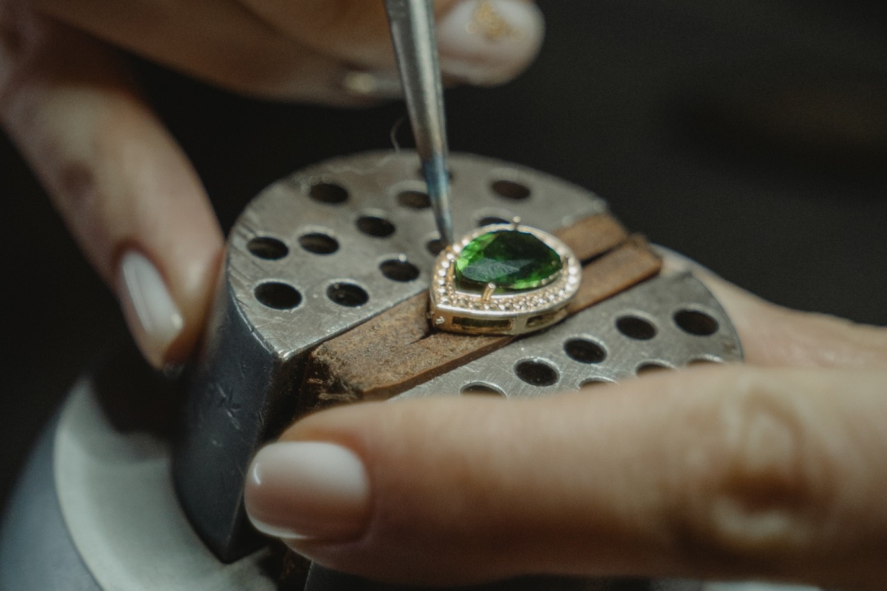 A close-up of a jeweller working on a piece with a green pear cut centre stone.