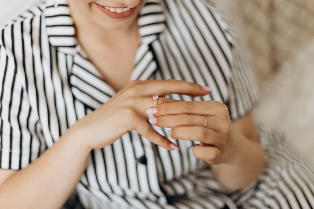 Woman smiling while wearing a diamond engagement ring, dressed in a striped shirt.