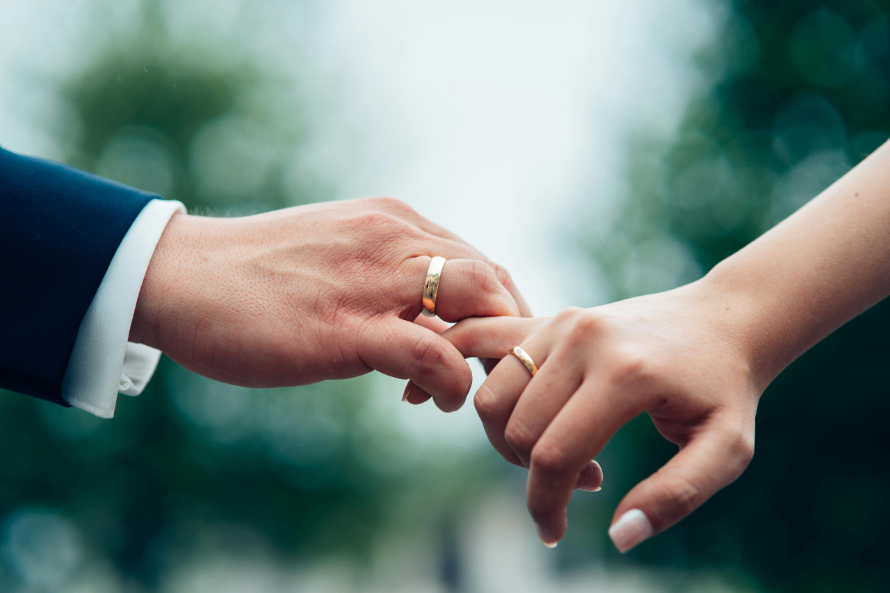 Two intertwining hands with yellow gold wedding bands.