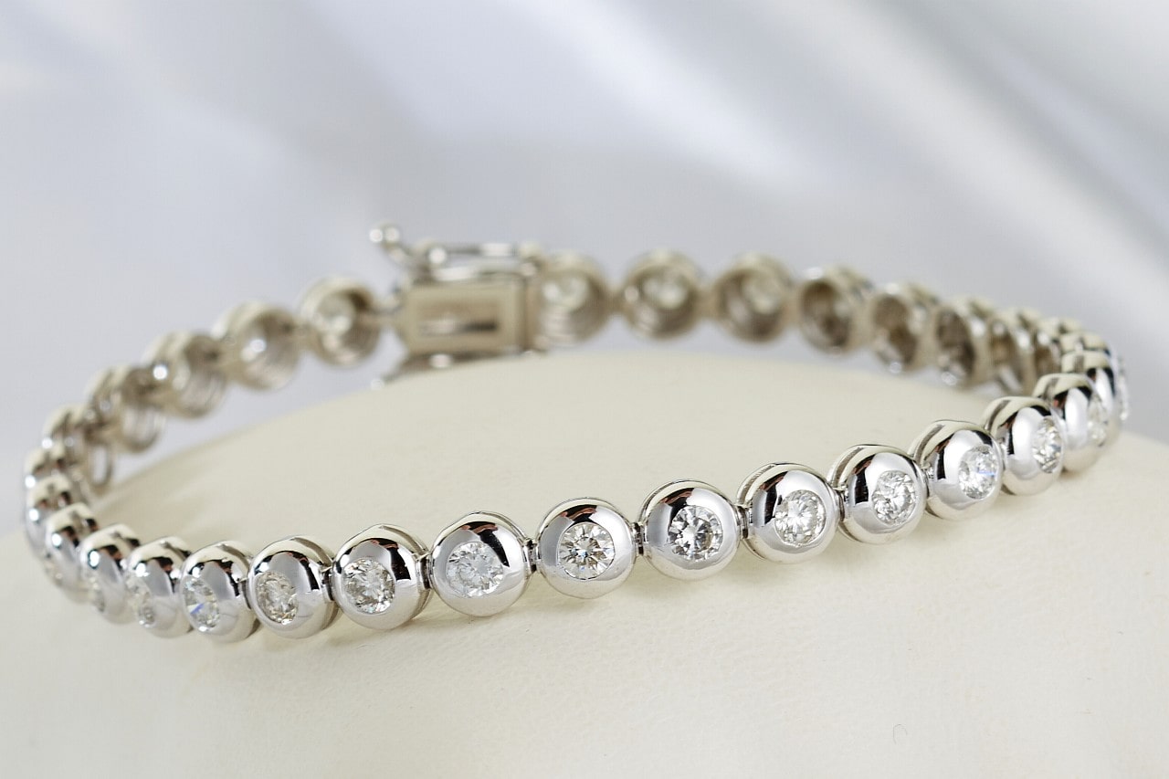 A silver diamond bezel set tennis bracelet on a white surface.