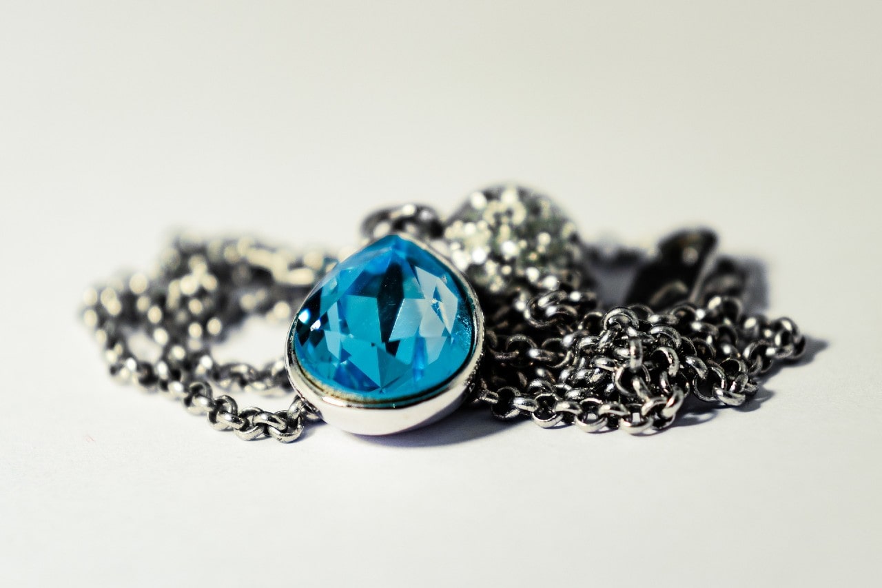 A sterling silver chain pendant with a pear shaped blue sapphire on a white surface.